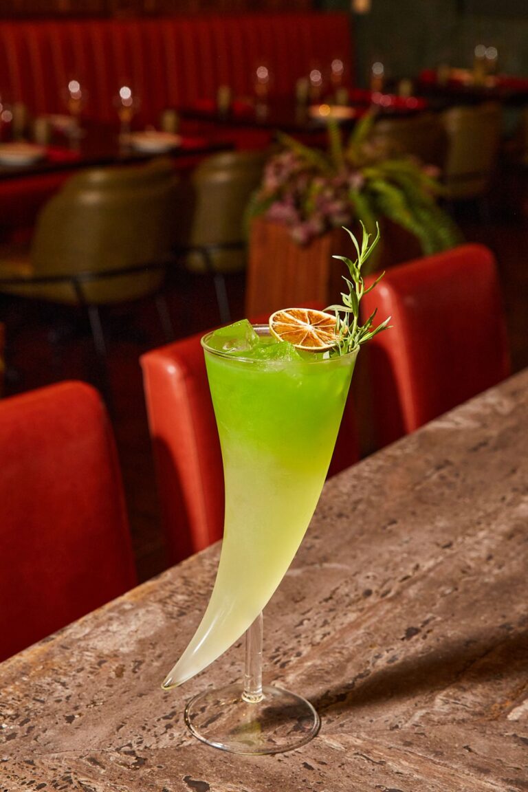 A green cocktail with a dried citrus garnish in a tall horn-shaped glass