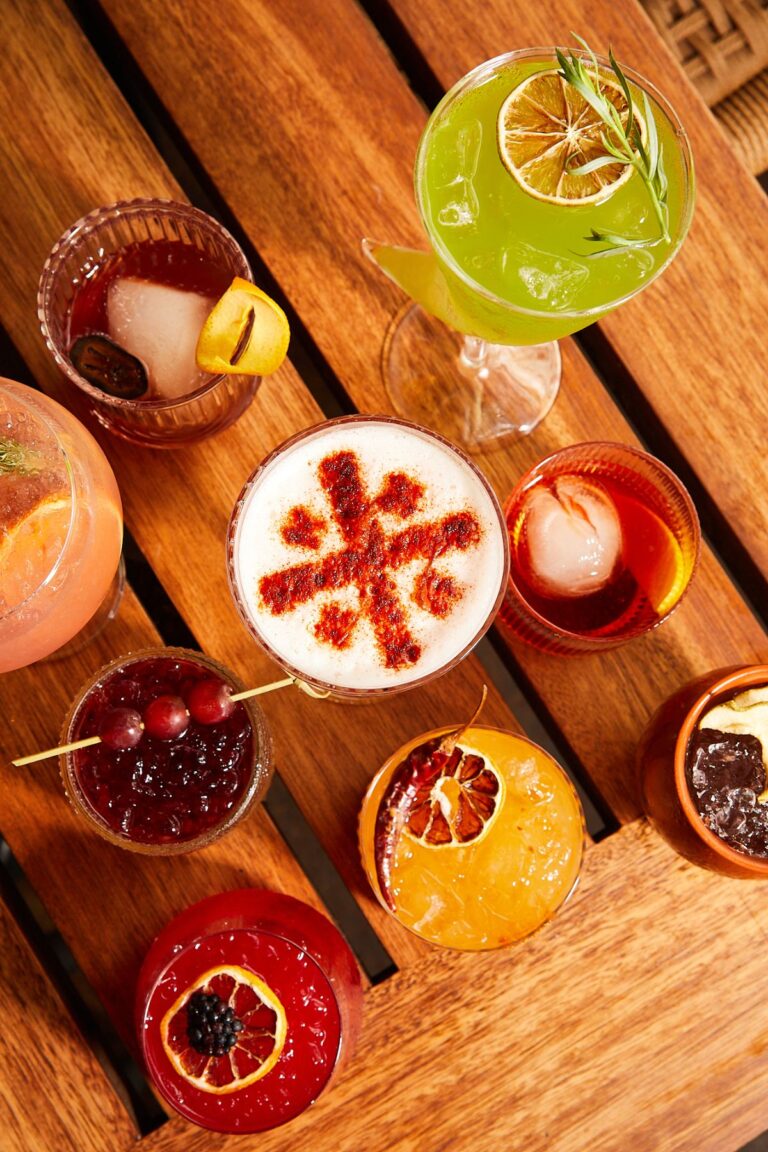 Overhead view of a spread of colorful cocktails on a wooden table