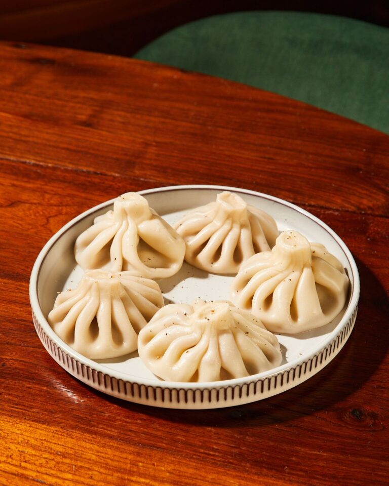 Six hand-folded khinkali dumplings on a white plate