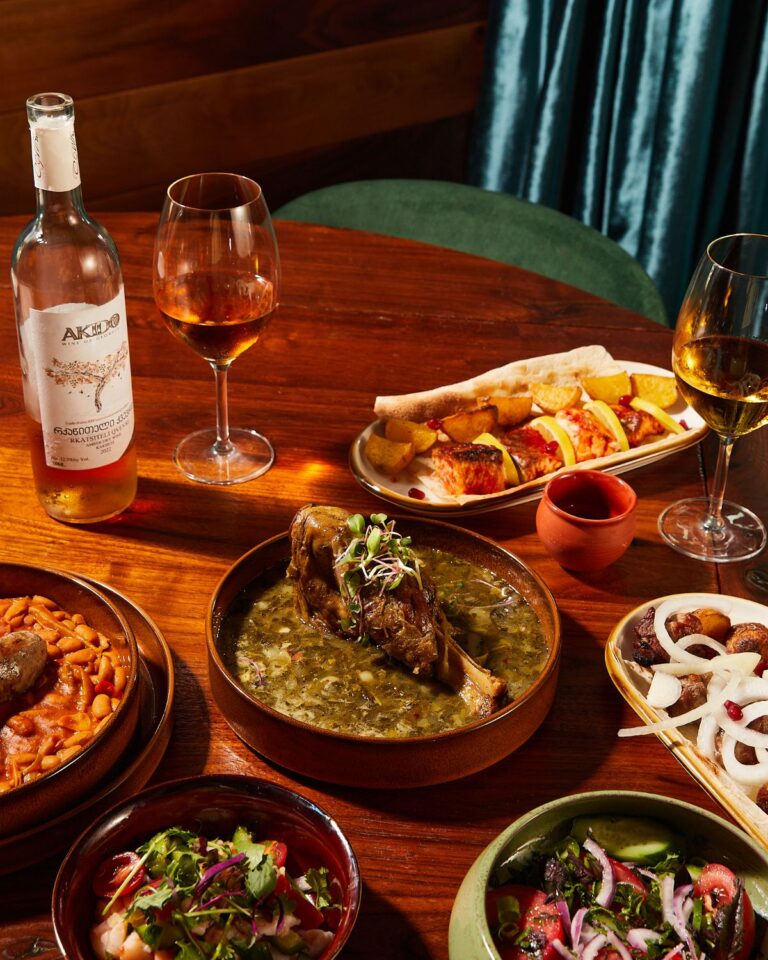 A table set with lamb shank, salads, khachapuri, and rosé wine