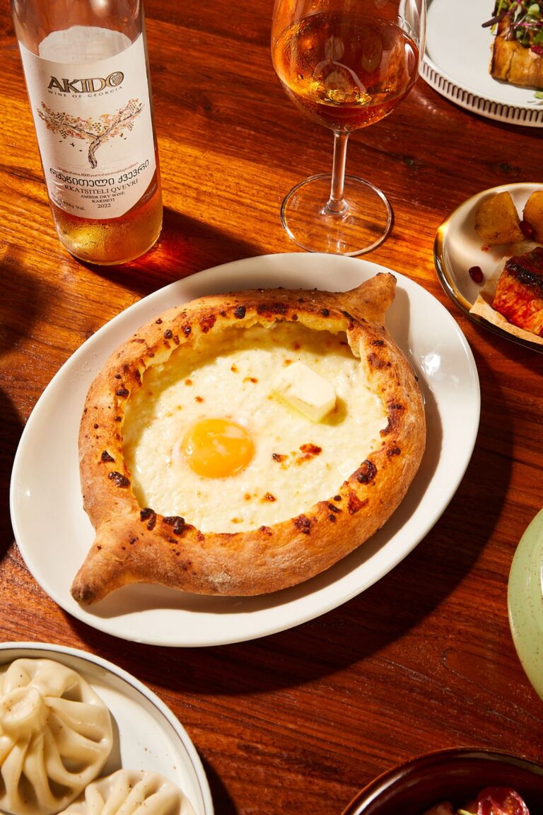 Adjaruli khachapuri, a boat-shaped cheese bread with a baked egg yolk, beside a bottle and glass of amber wine