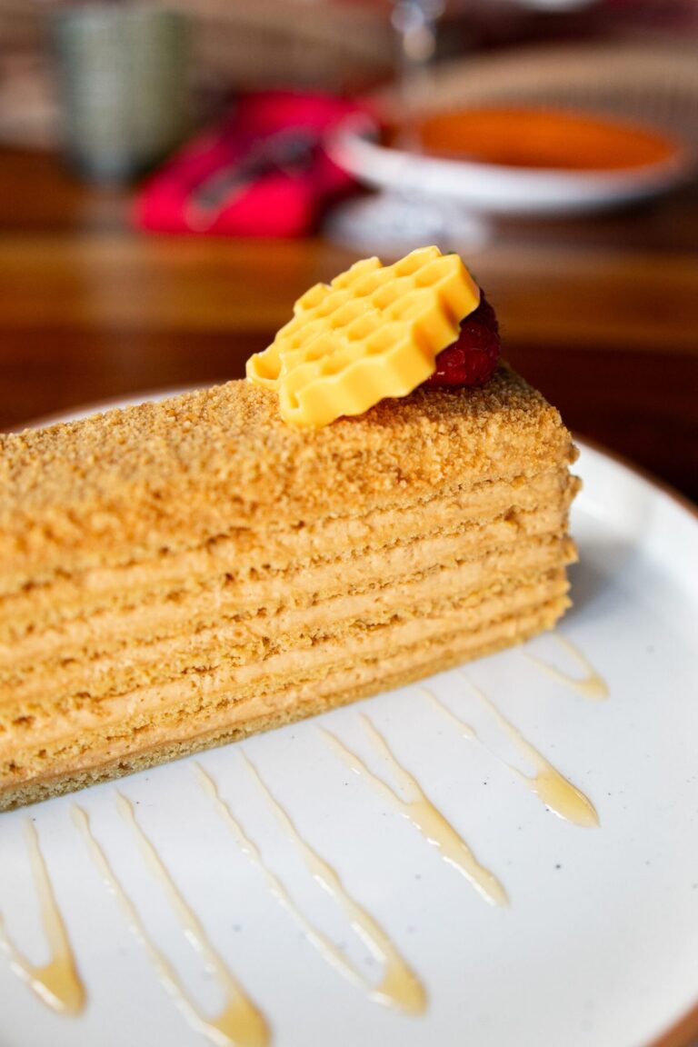 A slice of layered honey cake with a raspberry, mint, and a wafer garnish