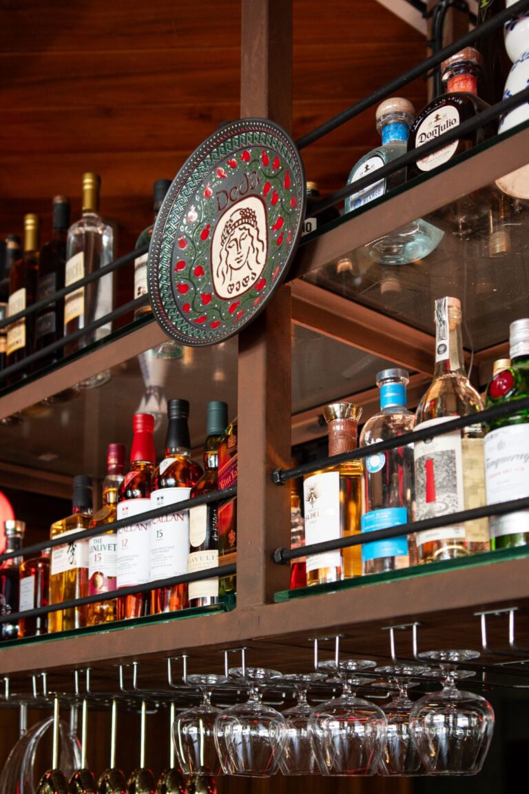 Bar with shelves of bottles, hanging glasses, and a round Deda sign