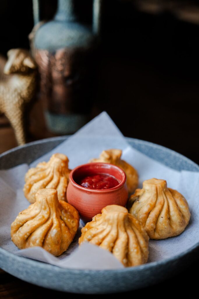 Pan-fried khinkali dumplings with a small bowl of red sauce on a blue plate