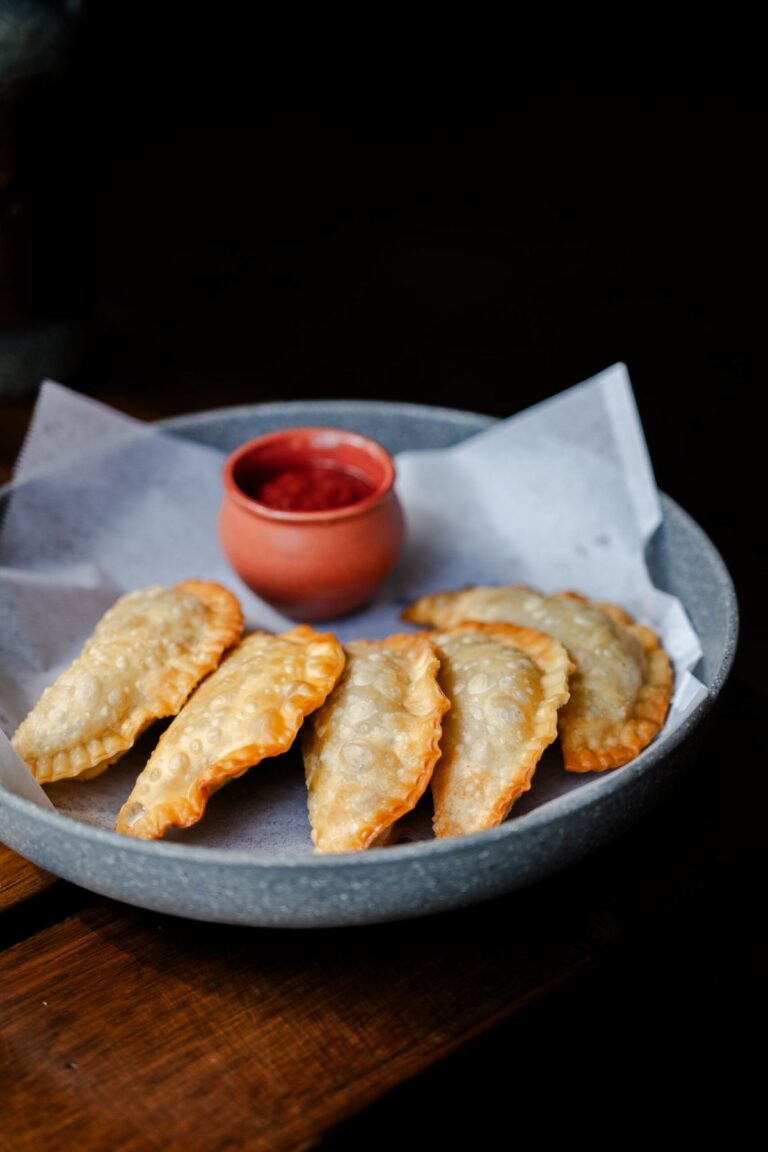 Pan-fried dumplings on a blue plate with a bowl of red dipping sauce